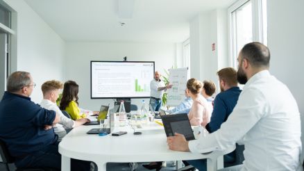 Schulung an einem Tisch mit Laptops und ein Trainer zeigt was am Flipchart