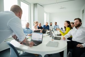Trainer im Vordergrund, an einem Tisch mit Schulungsteilnehmern
