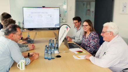 Ein Team von Fachleuten sitzt in einem Konferenzraum, diskutiert über Hafenlogistik und betrachtet eine Präsentation auf einem Bildschirm.