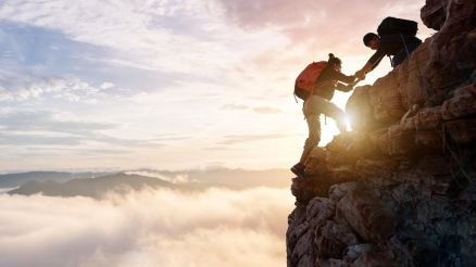 Personen helfen sich gemeinsam auf einen Berg zu steigen, stimmungsvoll mit Sonnenuntergang.