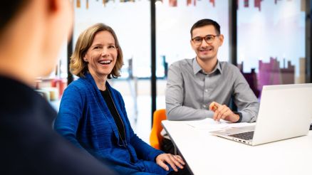 Drei Personen sitzen an einem Tisch und haben einen Laptop vor sich.